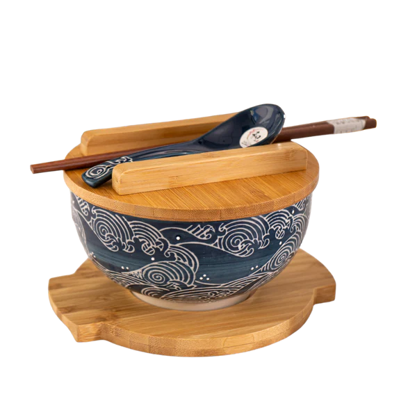 Blue ceramic wave-pattern bowl with bamboo lid, wooden trivet, chopsticks, and matching ceramic spoon.